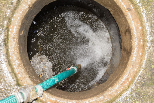 Hydro jet nozzle inserted into drain opening and spraying highly pressurized water.